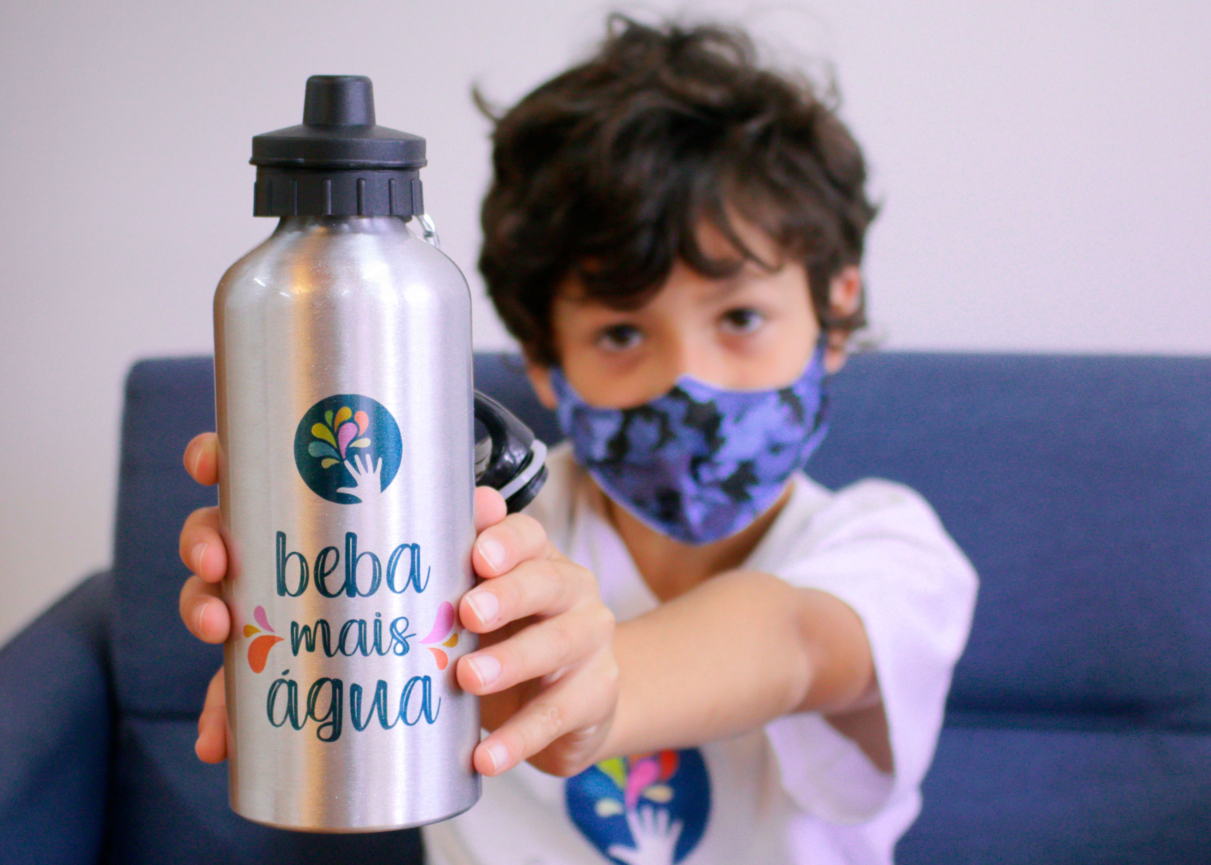Um menino usando máscara segura apontando para frente uma garrafa escrito beba mais água.
