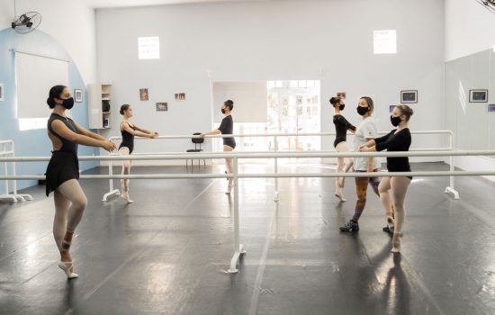 A imagem mostra alunas núcleo de dança tendo aula de ballet nas barras
